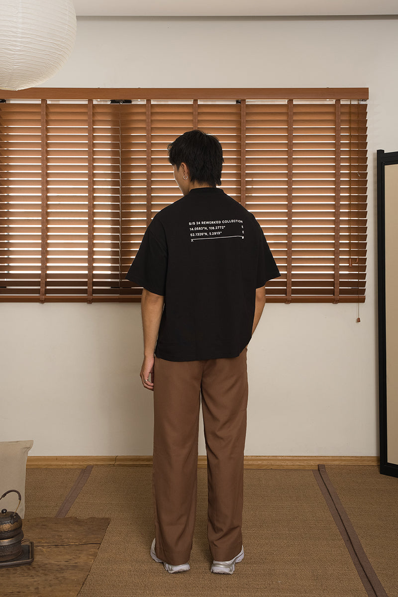 Person wearing a black t-shirt and brown pants standing in front of wooden blinds from the brand MINUS-E.